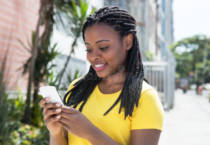 Afrikansk amerikankvinna i ett smsande meddelande för gul skjorta med mobiltelefonen