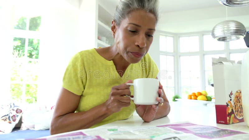 Afrikansk amerikankvinna som äter frukosten och den läs- tidningen stock video