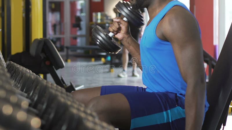 Afrikansk amerikanman som gör den omväxlande hantelelevatorn-upp, växande biceps, genomkörare