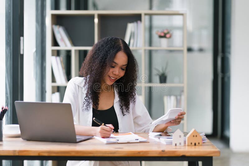 African american real estate agent examining housing market documents with calculator at office desk. African american real estate agent examining housing market documents with calculator at office desk.