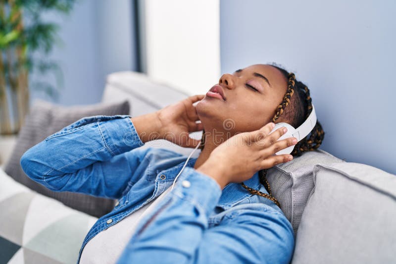 Afrikansk amerikansk kvinna som lyssnar på musik som sitter på soffan hemma arkivfoton