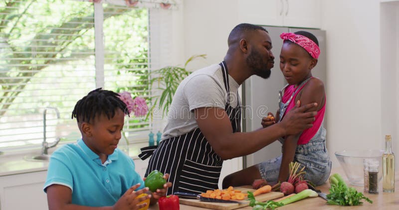 Afrikansk amerikansk pappa som omfamnar sina barn i köket hemma