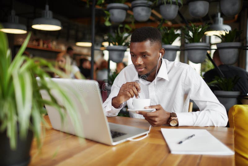 Afrikansk freelancerman som dricker kaffe som arbetar på kafét med bärbara datorn royaltyfri bild Afrikansk freelancerman som dricker kaffe som arbetar på kafét med bärbara datorn royaltyfri bild