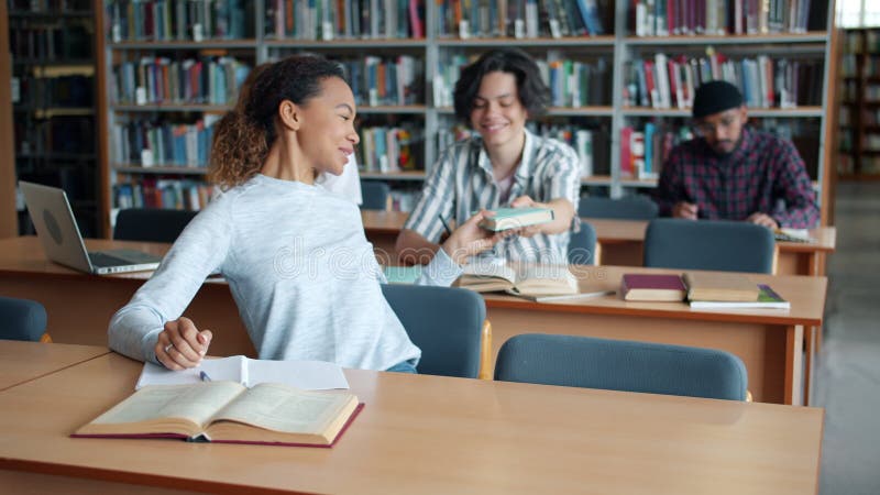 Afrikanska amerikanska flickor som studerar i bibliotek och läser bok från manliga studenter lager videofilmer
