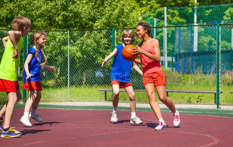 African girl holds ball and teenagers playing basketball on playground during summer. African girl holds ball and teenagers playing basketball on playground during summer