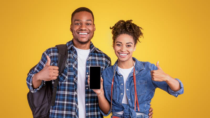Afrikanska resenärer: ett par som visar Smartphone-skärm som ger tummenUpp gul bakgrund royaltyfri foto