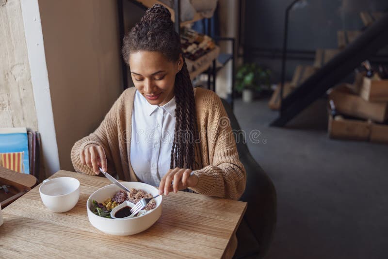 Afrique amérique jeune femme belle déjeuner dans un restaurant goûtant un plat sain servi dans un bol blanc photographie stock