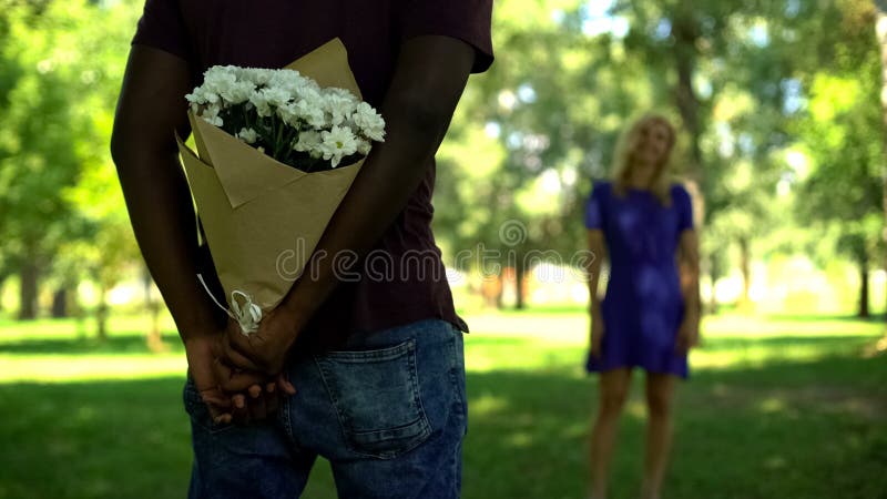 Afro-american boyfriend hiding flowers bouquet behind back in park, surprise stock image Afro-american boyfriend hiding flowers bouquet behind back in park, surprise stock image
