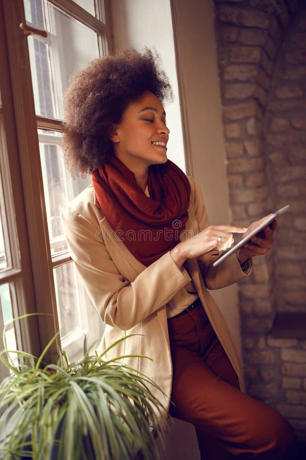 Afro-American girl with ipad standing near window in office