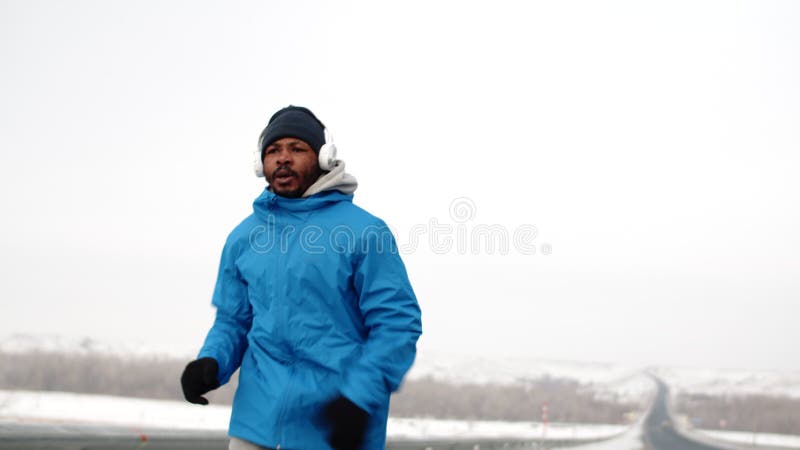 Afro-americano in abiti caldi corre lungo la strada per fare addestramento cardiaco e scappa dal frame front view. nero