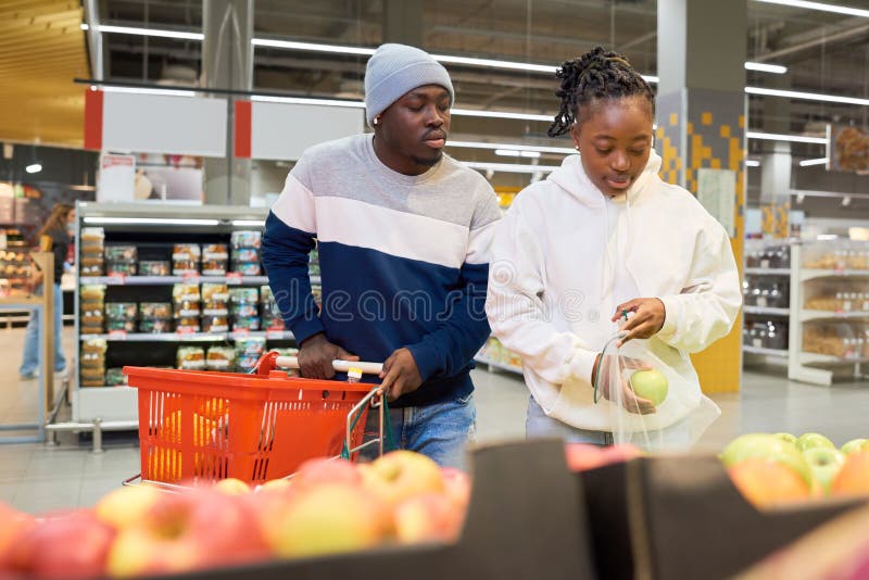 Afro-américain gars avec chariot debout par sa copine choisir des pommes fraîches