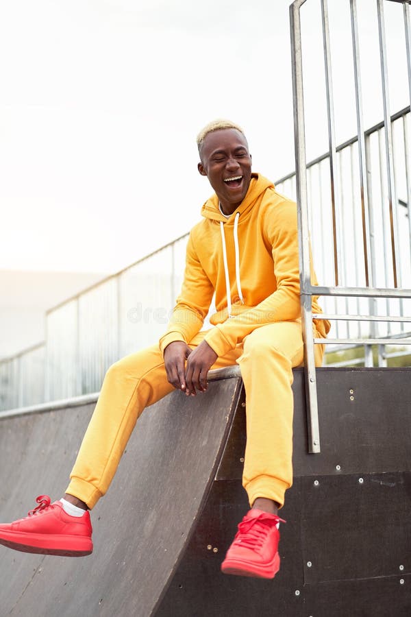 Afro-américain souriant noir homme jaune sweat à capuche extérieur heureux émotif afro modèle gars assis skate parc été jour espac