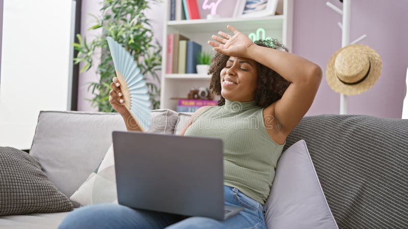 Afro-américaine femme avec ventilateur et ordinateur portable sur canapé à l'intérieur photos libres de droits