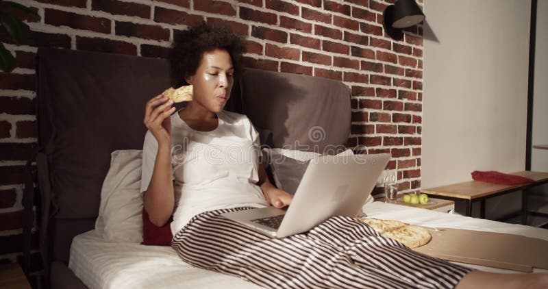 Afro-américaine mangeant de la pizza et utilisant un ordinateur portable clips vidéos