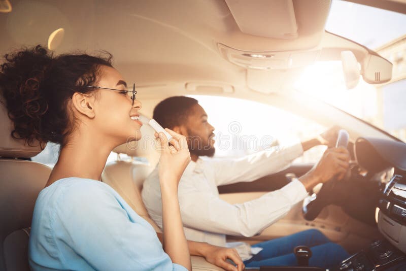Afro man driving car, his girlfriend applying lipstick stock photo Afro man driving car, his girlfriend applying lipstick stock photo