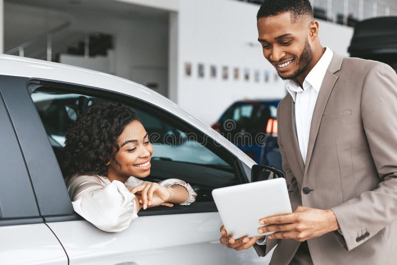 African American Woman Buying Car, Salesman Showing Papers And Documents Offering Deal In Auto Dealership Center. African American Woman Buying Car, Salesman Showing Papers And Documents Offering Deal In Auto Dealership Center.