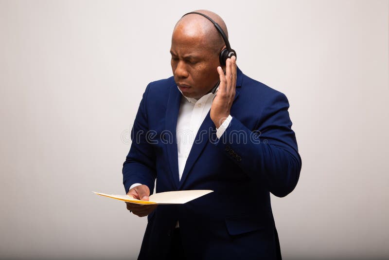 Afroamerikaner-Geschäftsmann Listens Through Headset während Holding-Datei lizenzfreie stockfotos Afroamerikaner-Geschäftsmann Listens Through Headset während Holding-Datei lizenzfreie stockfotos