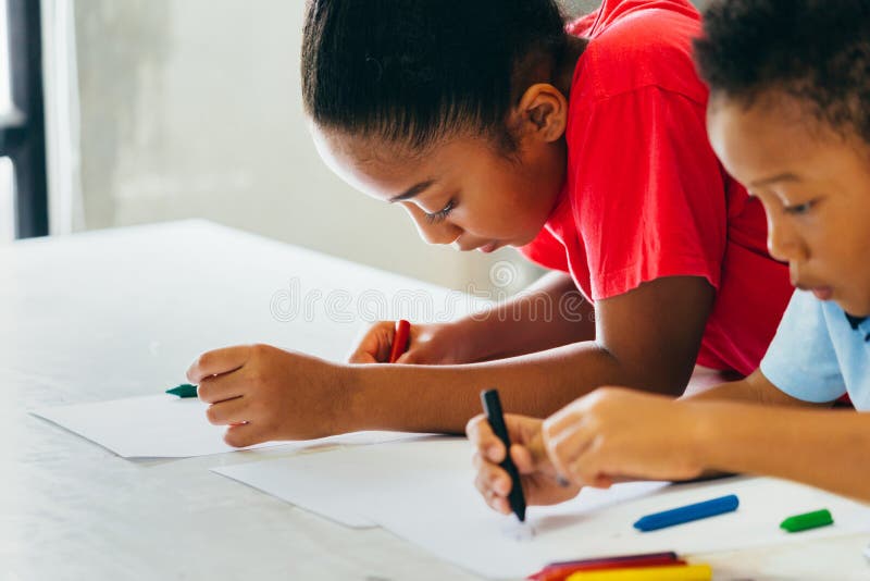 Afroamerikanerkinder, die wie man mit Zeichenstift auf Tabelle lernen, zeichnet