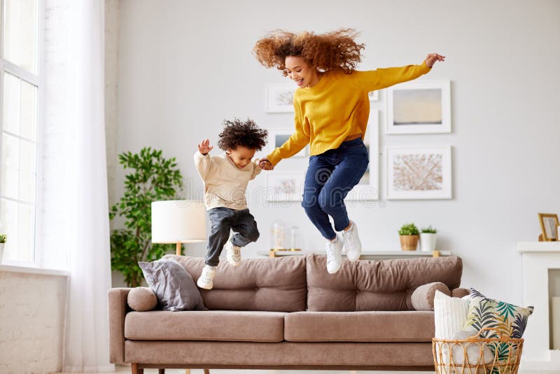 Crazy weekend with mom. Joyful afro american family mother and little son holding hands and jumping on sofa in living room at home, full length shot. Mom and child in casual wear playing together. Crazy weekend with mom. Joyful afro american family mother and little son holding hands and jumping on sofa in living room at home, full length shot. Mom and child in casual wear playing together