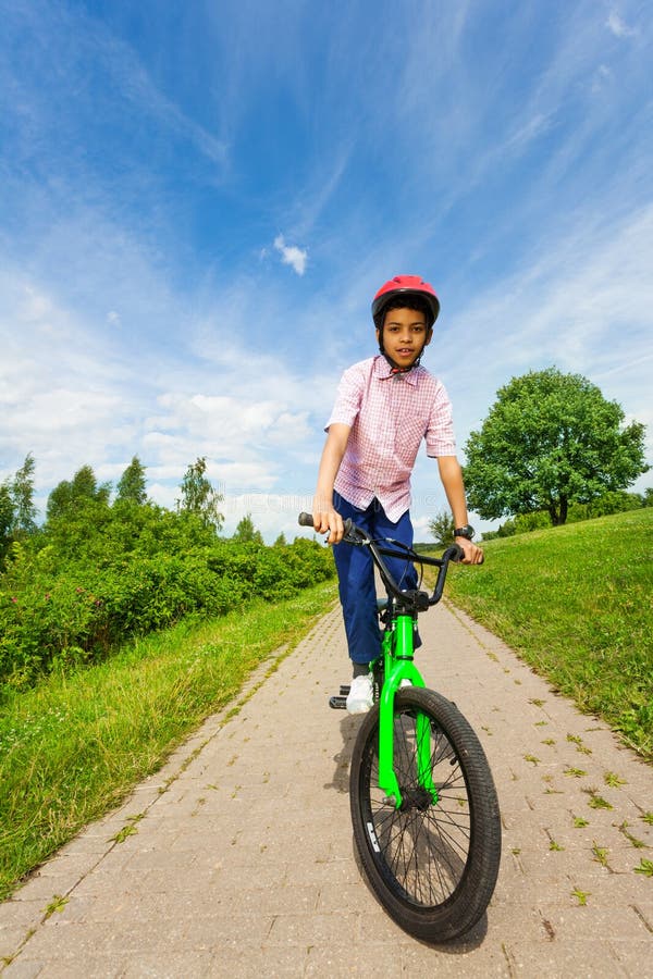 African boy in red helmet rides bright green bike along the road. African boy in red helmet rides bright green bike along the road.