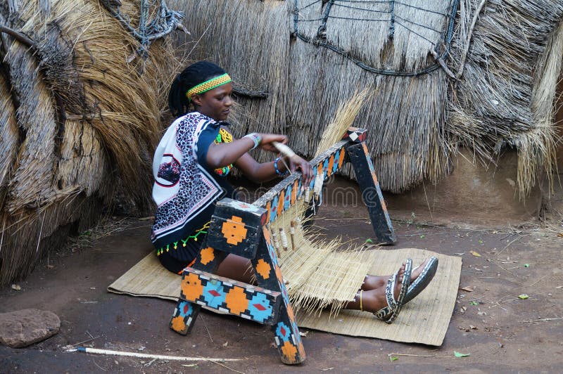 Lesedi Cultural Village, South Africa - 20 October 2016: Unidentified African Zulu woman wearing traditional handmade costume, weave straw carpet in Lesedi African Cultural village, South Africa. Lesedi Cultural Village, South Africa - 20 October 2016: Unidentified African Zulu woman wearing traditional handmade costume, weave straw carpet in Lesedi African Cultural village, South Africa