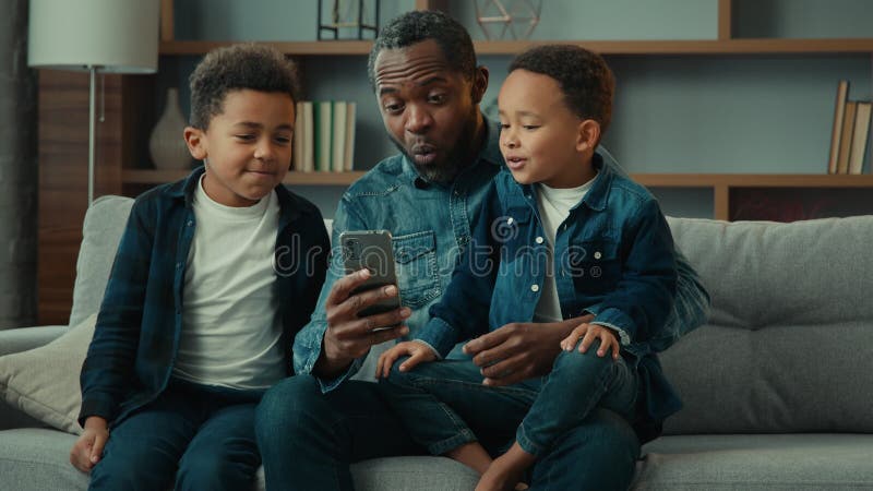 Afrykański amerykański ojciec dorosłej rodziny z dwójką dzieci dzieci dzieci chłopcy dzieci na kanapie używają zabawnych aplikacji