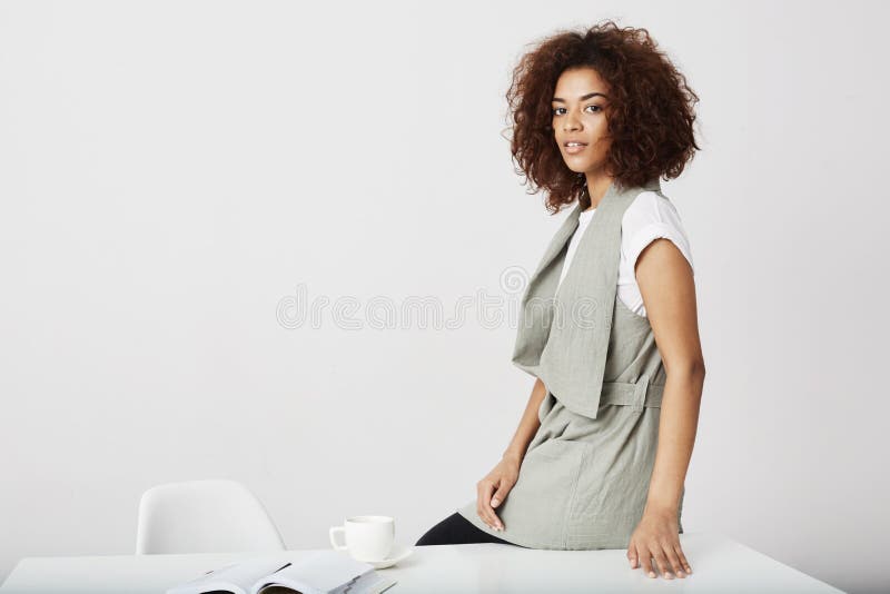 Afrykańskiego bizneswomanu uśmiechnięty obsiadanie na stole przy miejscem pracy nad białym tłem zdjęcie royalty free Afrykańskiego bizneswomanu uśmiechnięty obsiadanie na stole przy miejscem pracy nad białym tłem zdjęcie royalty free