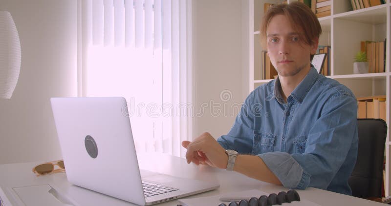 Afsluiten van het portret van een jonge, succesvolle kaukasische zakenman die een laptop gebruikt die binnen een camera op kantoor