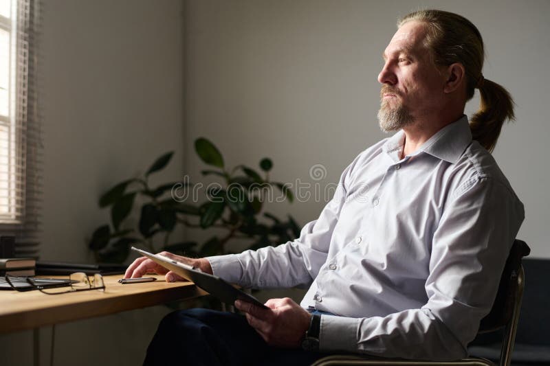 Aged man in shirt thinking of something by his workplace in office stock image