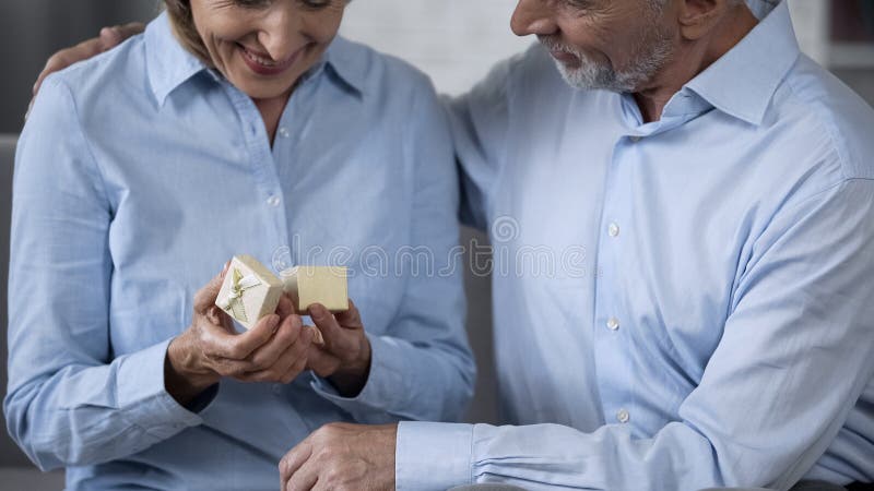 Aged woman smiling and holding small present box, man hugging her, anniversary royalty free stock photos Aged woman smiling and holding small present box, man hugging her, anniversary royalty free stock photos