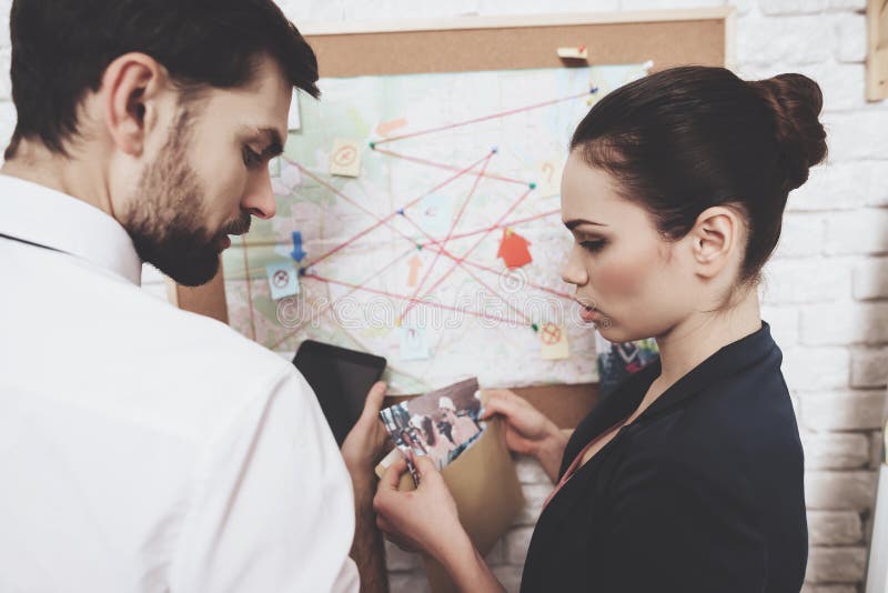 Agence de détectives privés L'homme et la femme regardent la carte, discutant des indices photo stock Agence de détectives privés L'homme et la femme regardent la carte, discutant des indices photo stock