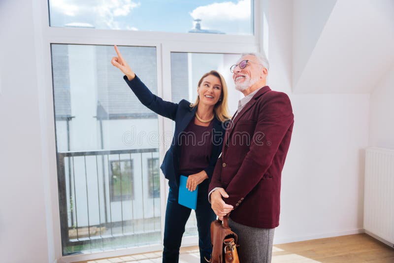 agent immobilier attrayant aux cheveux blonds montrant la grande fenêtre gentille dans la maison moderne images stock agent immobilier attrayant aux cheveux blonds montrant la grande fenêtre gentille dans la maison moderne images stock
