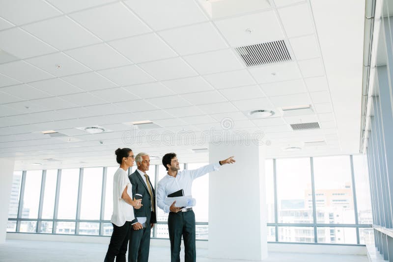 Real estate broker showing office space to clients. Business people and real estate agent at empty office space, with estate broker pointing at something interesting. Real estate broker showing office space to clients. Business people and real estate agent at empty office space, with estate broker pointing at something interesting.