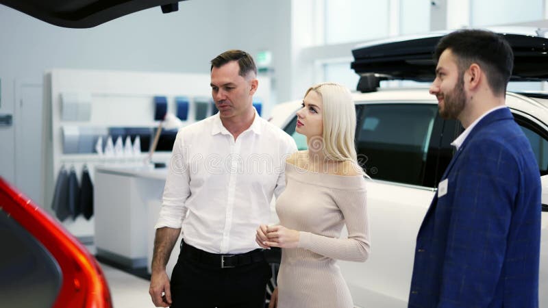 Agente de coches mostrando baúl a los clientes coche en sala de exposición de distribuidores de automóviles metrajes