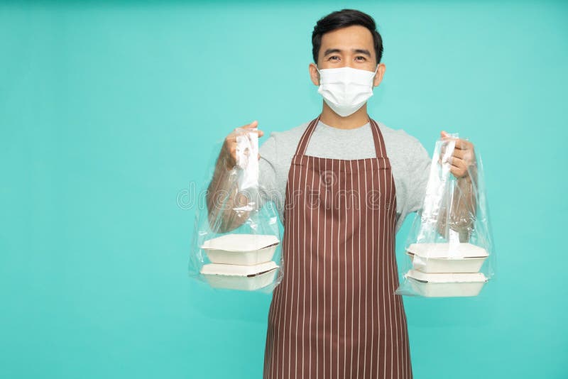 Agenți locali asiatici pentru restaurante cu mască față cu șorț maro în picioare și cu sac din plastic cu cutie pentru alimente. royalty free stock photography