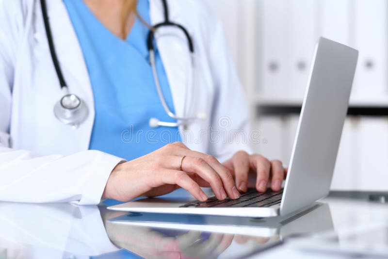 Aggiusti la battitura a macchina sul computer portatile mentre si siedono allo scrittorio di vetro nell'ufficio dell'ospedale Med fotografia stock Aggiusti la battitura a macchina sul computer portatile mentre si siedono allo scrittorio di vetro nell'ufficio dell'ospedale Med fotografia stock