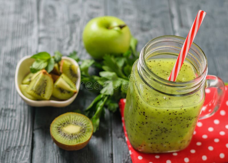 Aggredisca con il frullato appena fatto del kiwi su uno straccio e una mela e un prezzemolo rossi su una tavola nera rustica fotografia stock libera da diritti