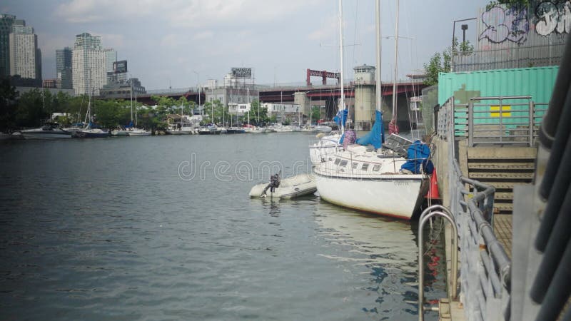 Aging white single hull sailboat with adjacent parked dinghy sits parked along the canal wall in Greenpoint Brooklyn