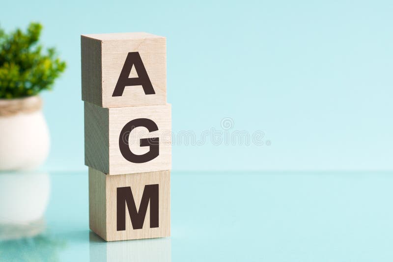 AGM Annual general meeting acronym on wooden cubes on blue backround. Business concept. Front view concepts, flower in the background. AGM Annual general meeting acronym on wooden cubes on blue backround. Business concept. Front view concepts, flower in the background