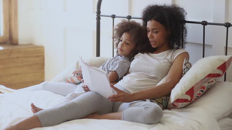 Agradable mujer birracial leyendo libro a su hija