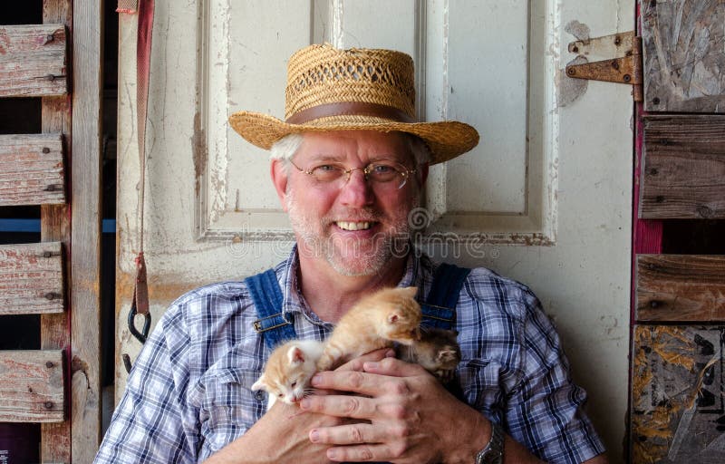 A smiling farmer in a straw hat holds an armful of tiny new kittens. A smiling farmer in a straw hat holds an armful of tiny new kittens