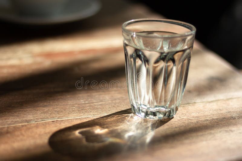 Agua en vidrio en la tabla de madera con la sombra, sol de la mañana fotografía de archivo libre de regalías Agua en vidrio en la tabla de madera con la sombra, sol de la mañana fotografía de archivo libre de regalías