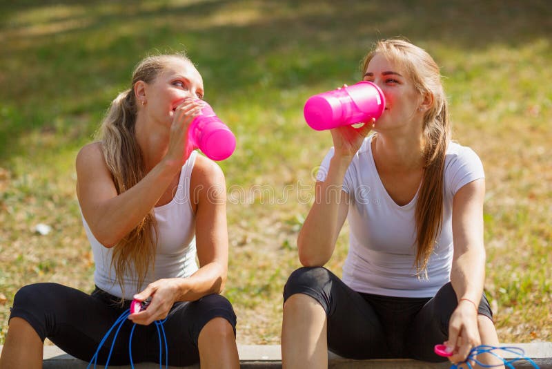 Agua potable de las chicas jóvenes felices después de un entrenamiento en un fondo natural Concepto sano de la forma de vida imagen de archivo libre de regalías Agua potable de las chicas jóvenes felices después de un entrenamiento en un fondo natural Concepto sano de la forma de vida imagen de archivo libre de regalías
