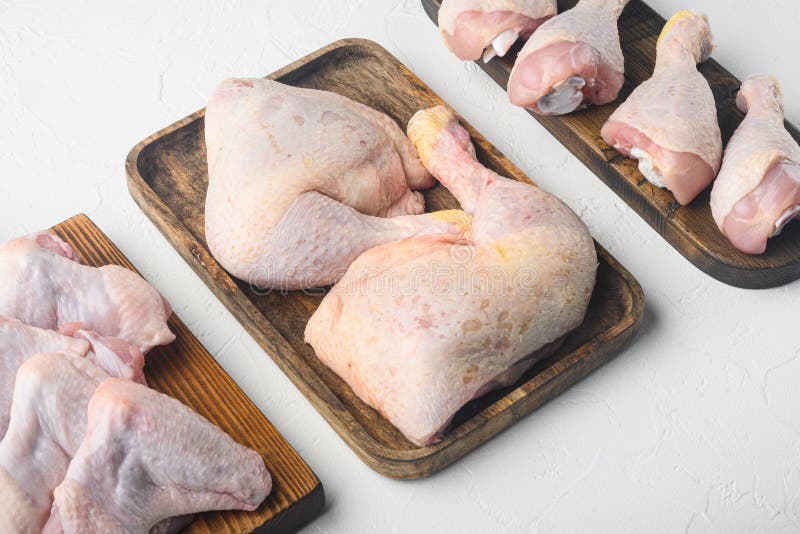 Raw chicken meat fillet, thigh, wings and legs set, on wooden cutting board, on white background. Raw chicken meat fillet, thigh, wings and legs set, on wooden cutting board, on white background