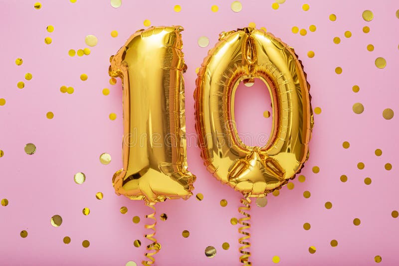 10 air balloon numbers on pink background. 10 k gold foil balloons with confetti. Birthday party flat lay with copy space