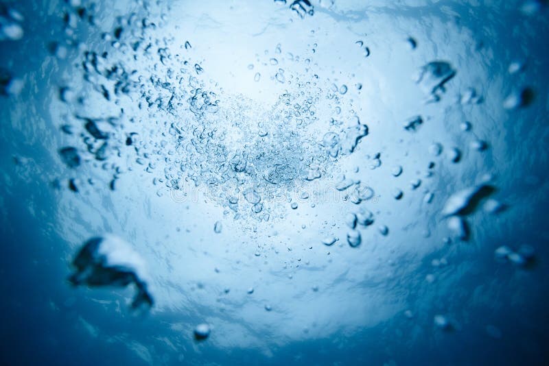 Air bubbles rising in blue water, underwater diving concept.