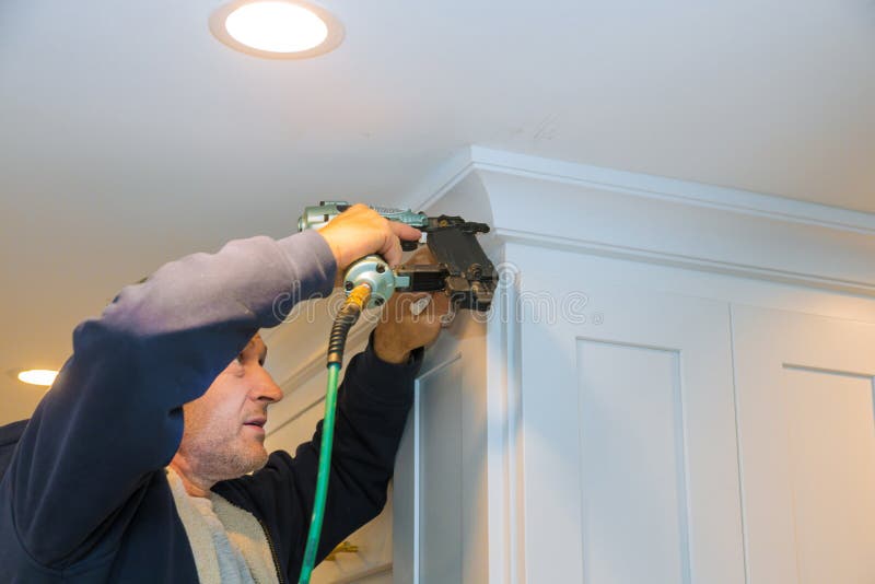 Air nailer tool carpenter using nail gun to crown moldings on kitchen cabinets with white cabinets