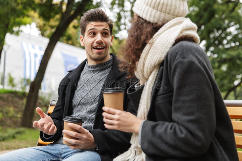 Aire libre de consumición del té o del café de los pares cariñosos jovenes felices en el parque que habla con uno a foto de archivo Aire libre de consumición del té o del café de los pares cariñosos jovenes felices en el parque que habla con uno a foto de archivo