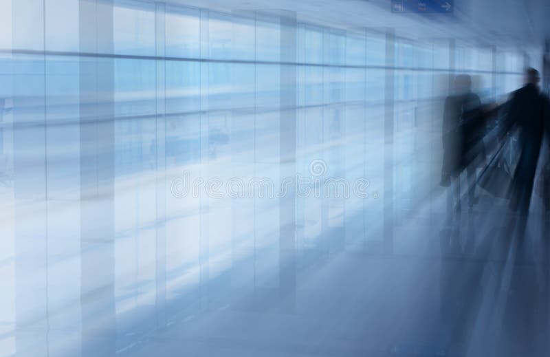 An interior view of passengers walking along a corridor of a busy international airport. An interior view of passengers walking along a corridor of a busy international airport.