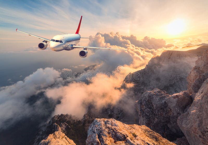 Airplane is flying over clouds at sunset. Landscape with white passenger airplane, mountains, sea and orange sky with sun in summer. Passenger aircraft is landing. Business travel. Commercial plane. Airplane is flying over clouds at sunset. Landscape with white passenger airplane, mountains, sea and orange sky with sun in summer. Passenger aircraft is landing. Business travel. Commercial plane